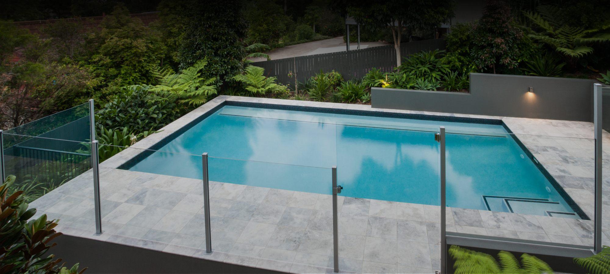 Minimalistic pool area design with a sleek glass fence and a fenceless pool area overlooking the garden