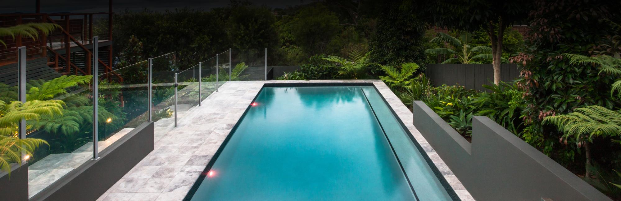 Minimalistic pool area design with a sleek glass fence and a fenceless pool area overlooking the garden