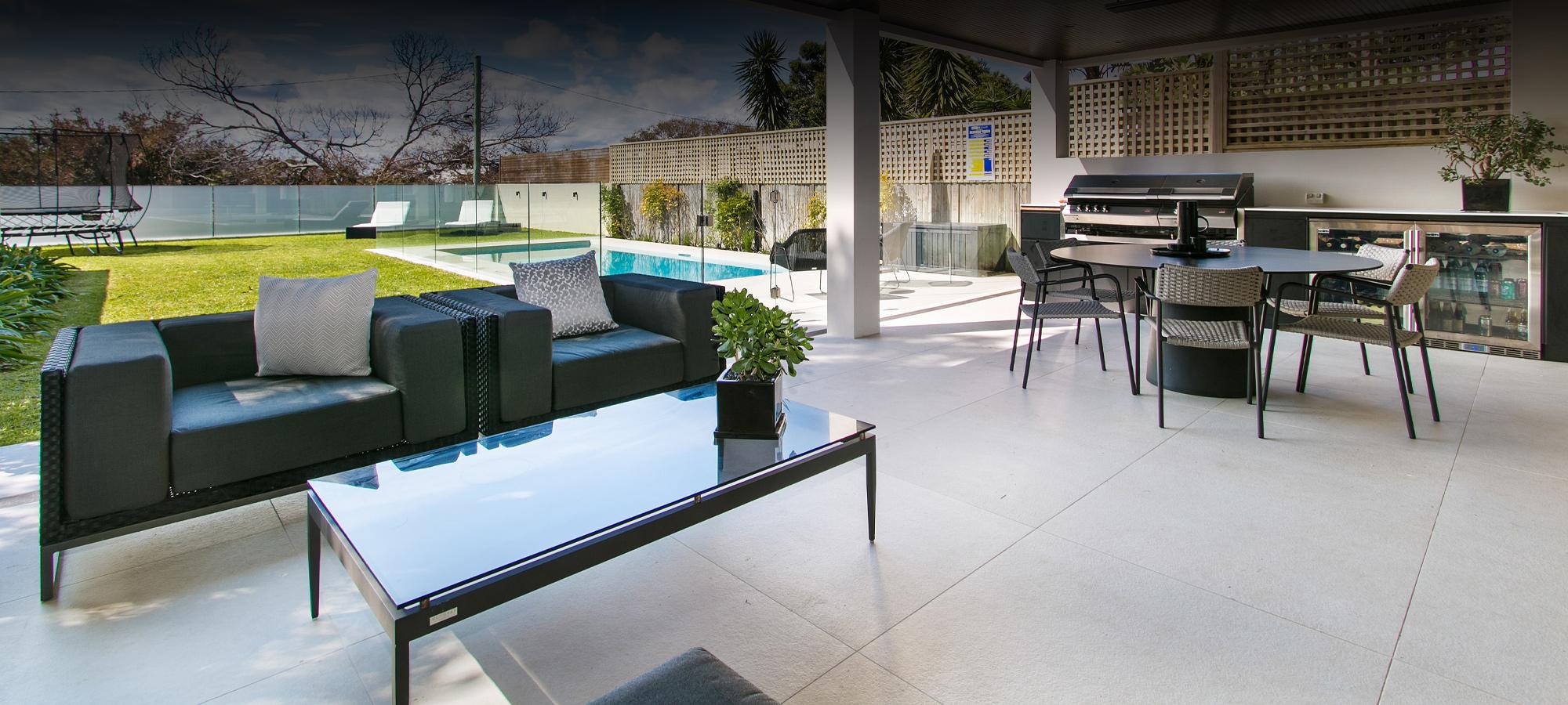 Massive outdoor area with a dining area and a couple outdoor lounging seats with a trampoline and a neat medium-sized pool in the background