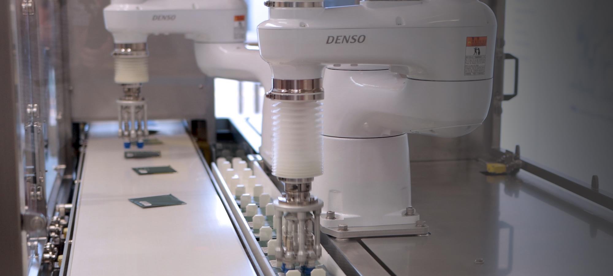 Large white automated industrial machines lifting product on to a factory conveyor belt 