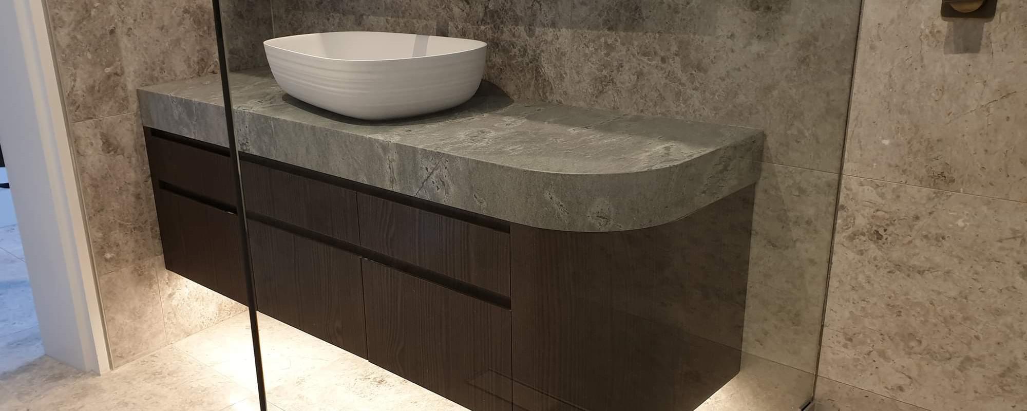 Floating bathroom basin with a grey marble benchtop, elevated white sink and dark wooden draws