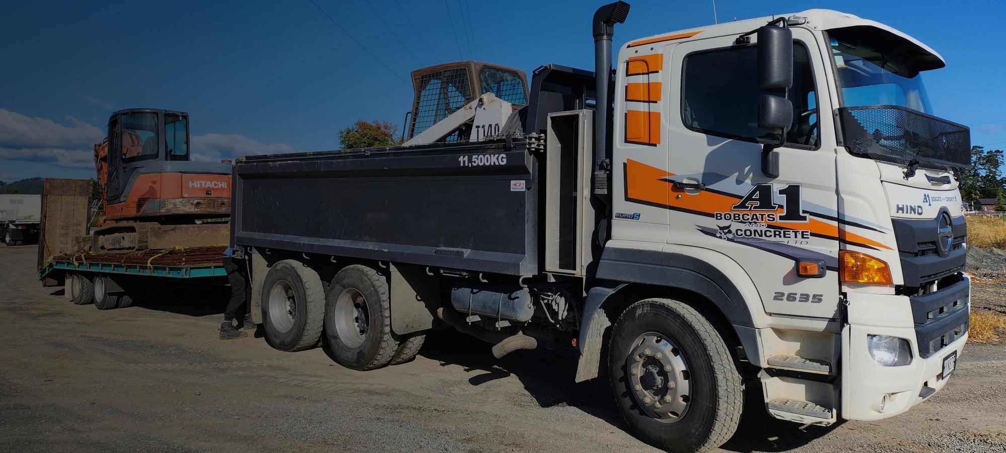 White and orange A1 Bobcats & Concrete earthmoving truck transporting several pieces of heavy machinery 