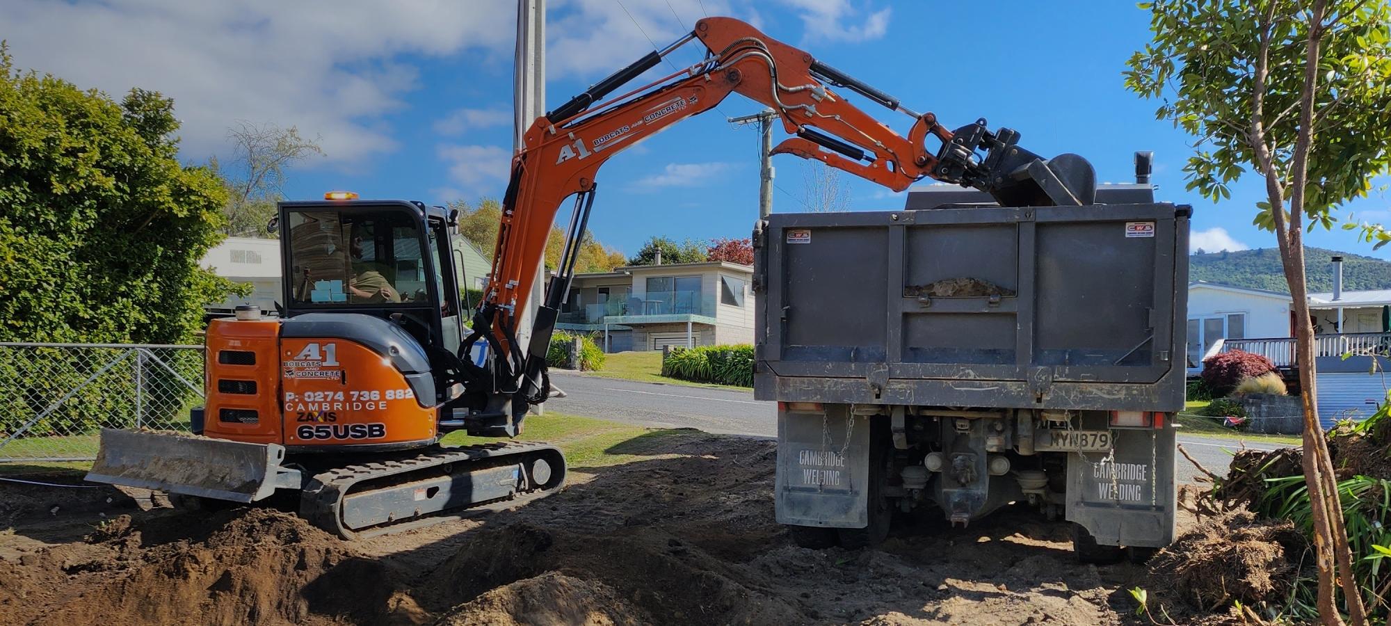 Orange earthmoving digger unloading dirt from a site they're levelling and making ready for building foundations