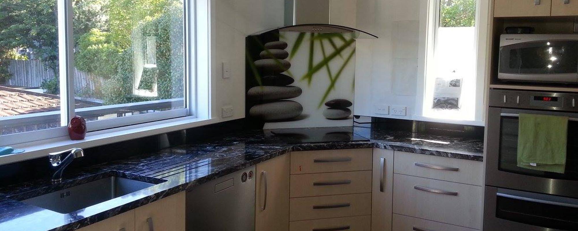 Tan coloured cabinetry and a black polished granite benchtop with a custom splashback on the wall with piled up rocks and green leaves on it