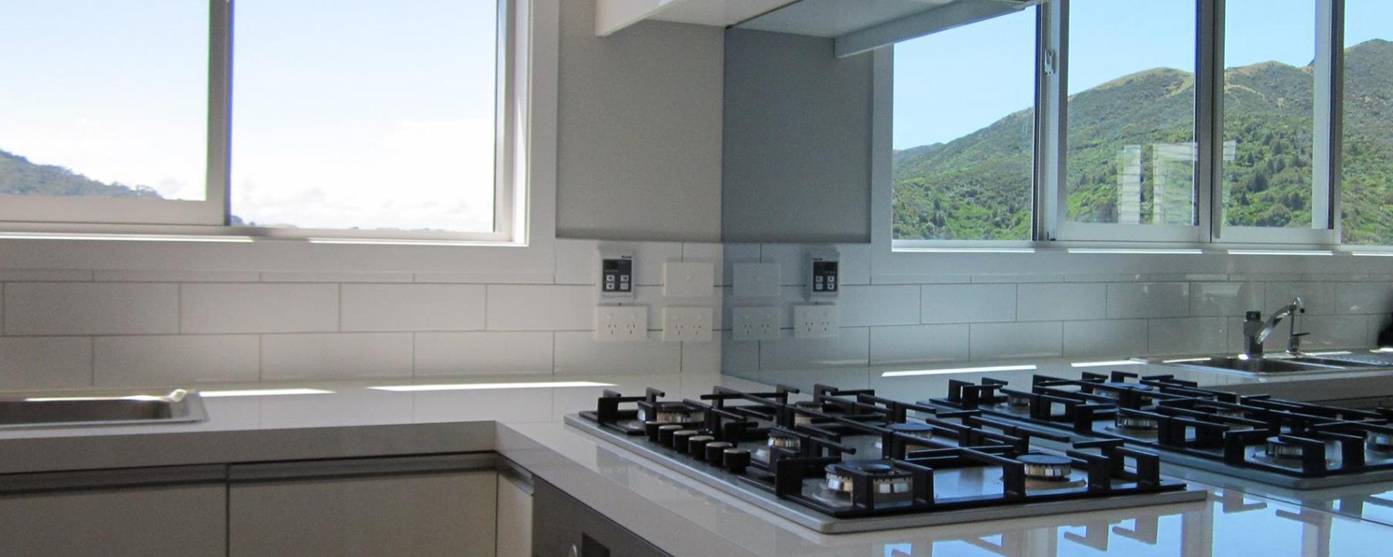 Classy white kitchen with a gas stovetop, white glossy benchtop, and a mirror splashback