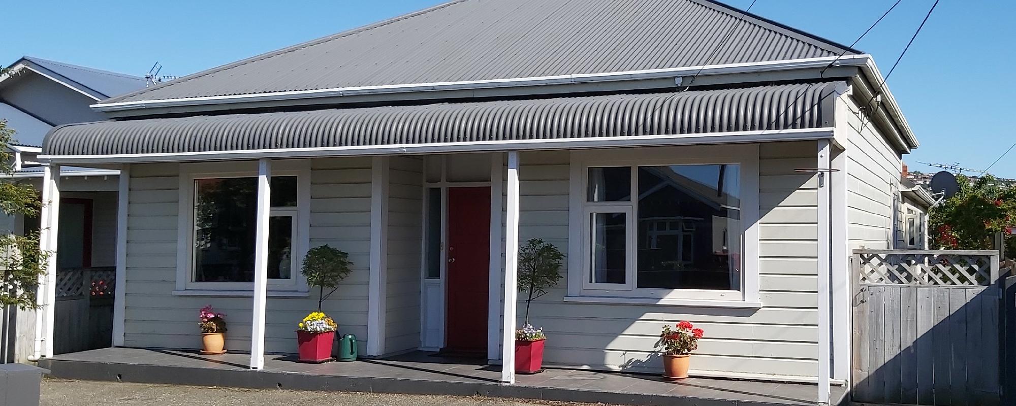 Off-white weatherboard home with a grey roof and white uPVC framing around the windows and entrance