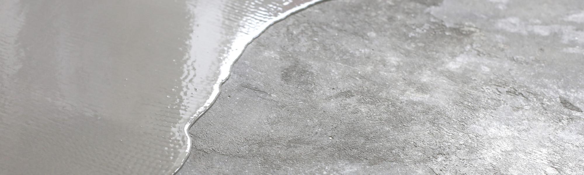 Concrete coloured liquid being spread across an old concrete floor