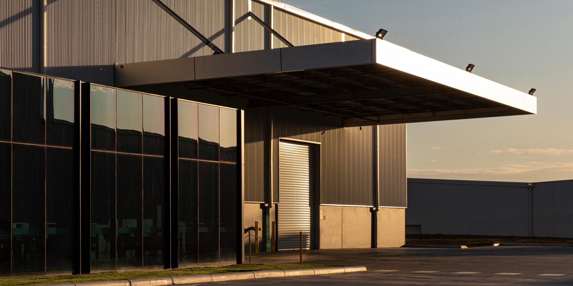 Large industrious commercial building with floor to ceiling windows, a large canopy that covers a tall commercial garage door
