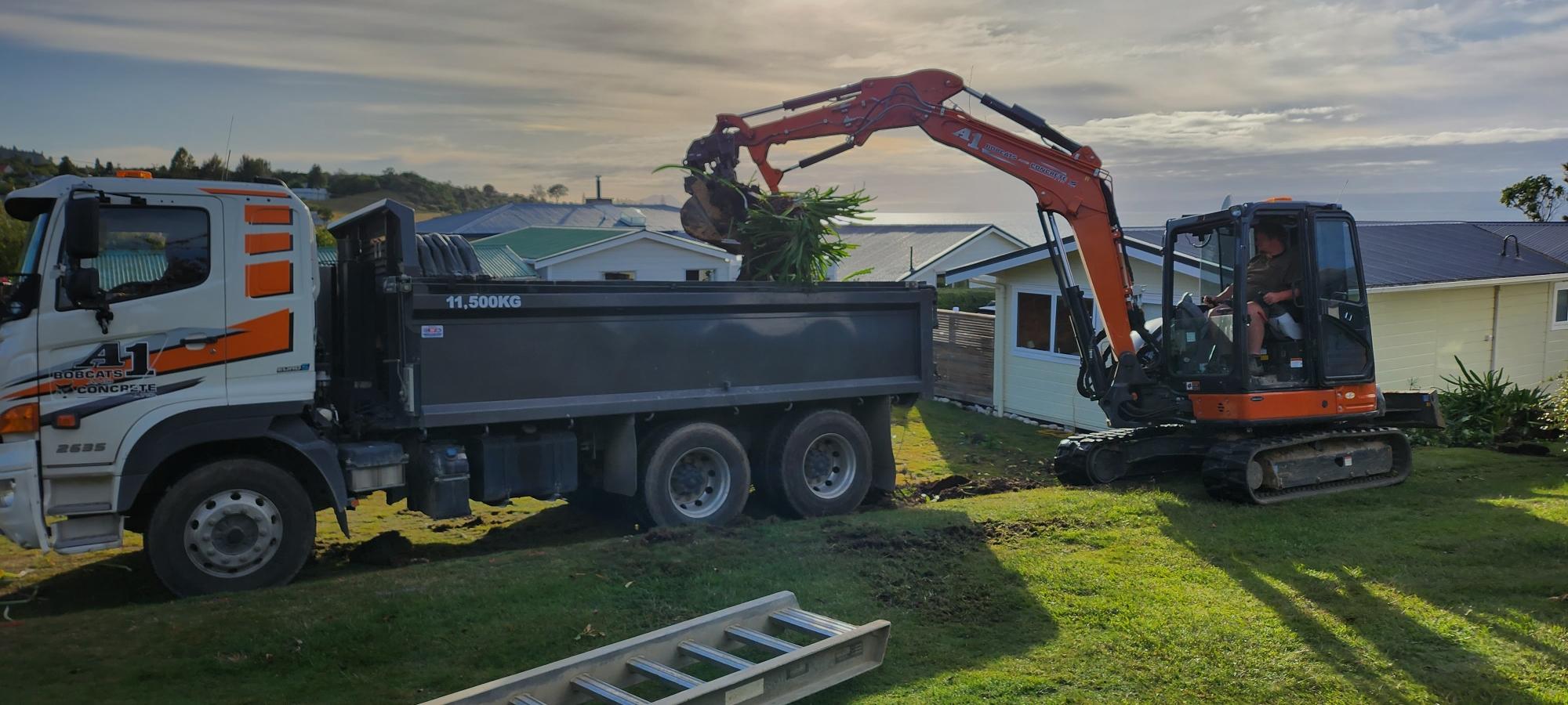 Little orange digger unloading plant debris from a site they're demolishing to unclutter the client's yard 