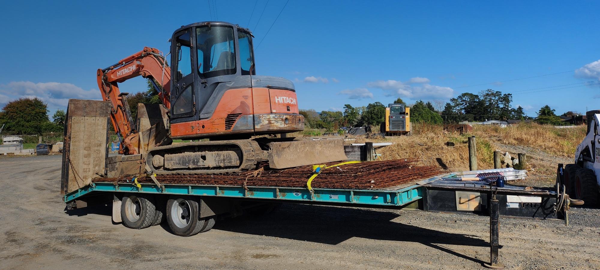 Little orange digger on the back of a long trailer ready to be unloaded and used for equipment hire