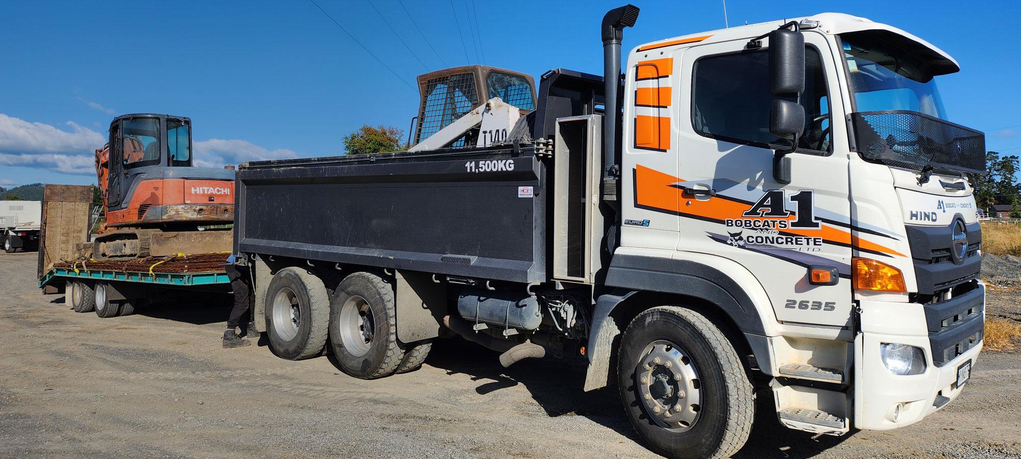 White and orange A1 Bobcats & Concrete earthmoving truck transporting several pieces of heavy machinery 