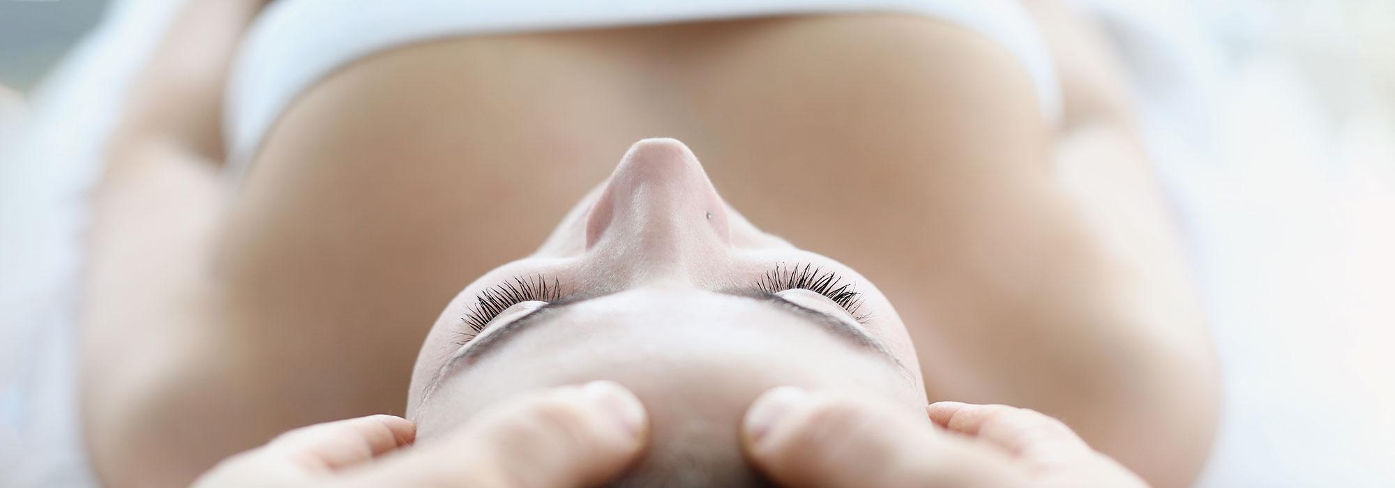 Woman wrapped in a towel, laying down on a comfy spa bed with her eyes closed as someone massages her head
