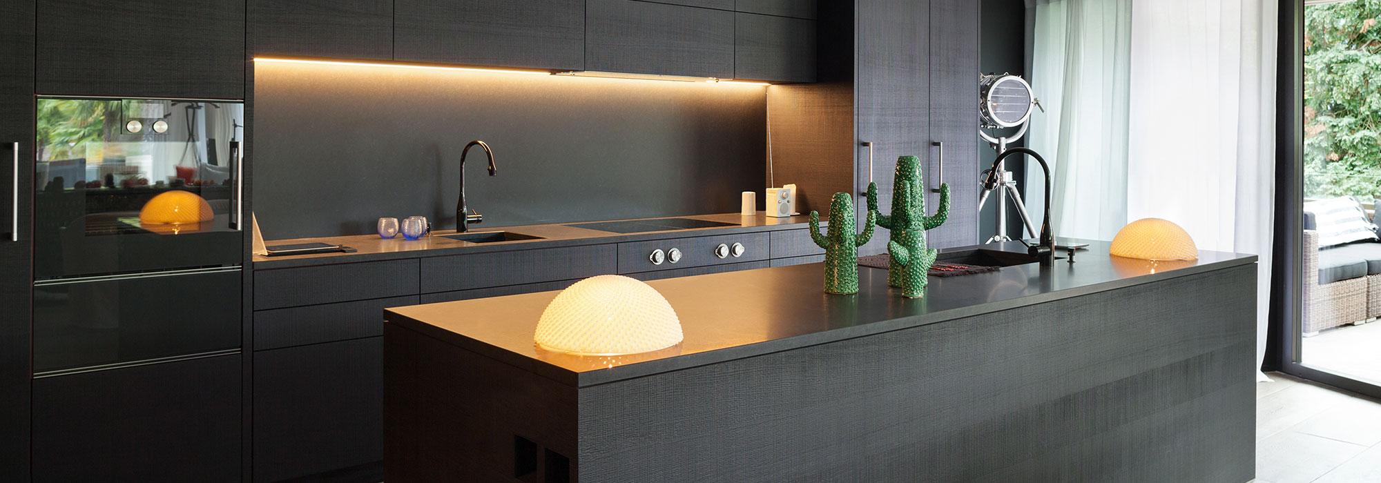 Dark black kitchen with cosy yellow lighting and a family of green cacti on the island bench