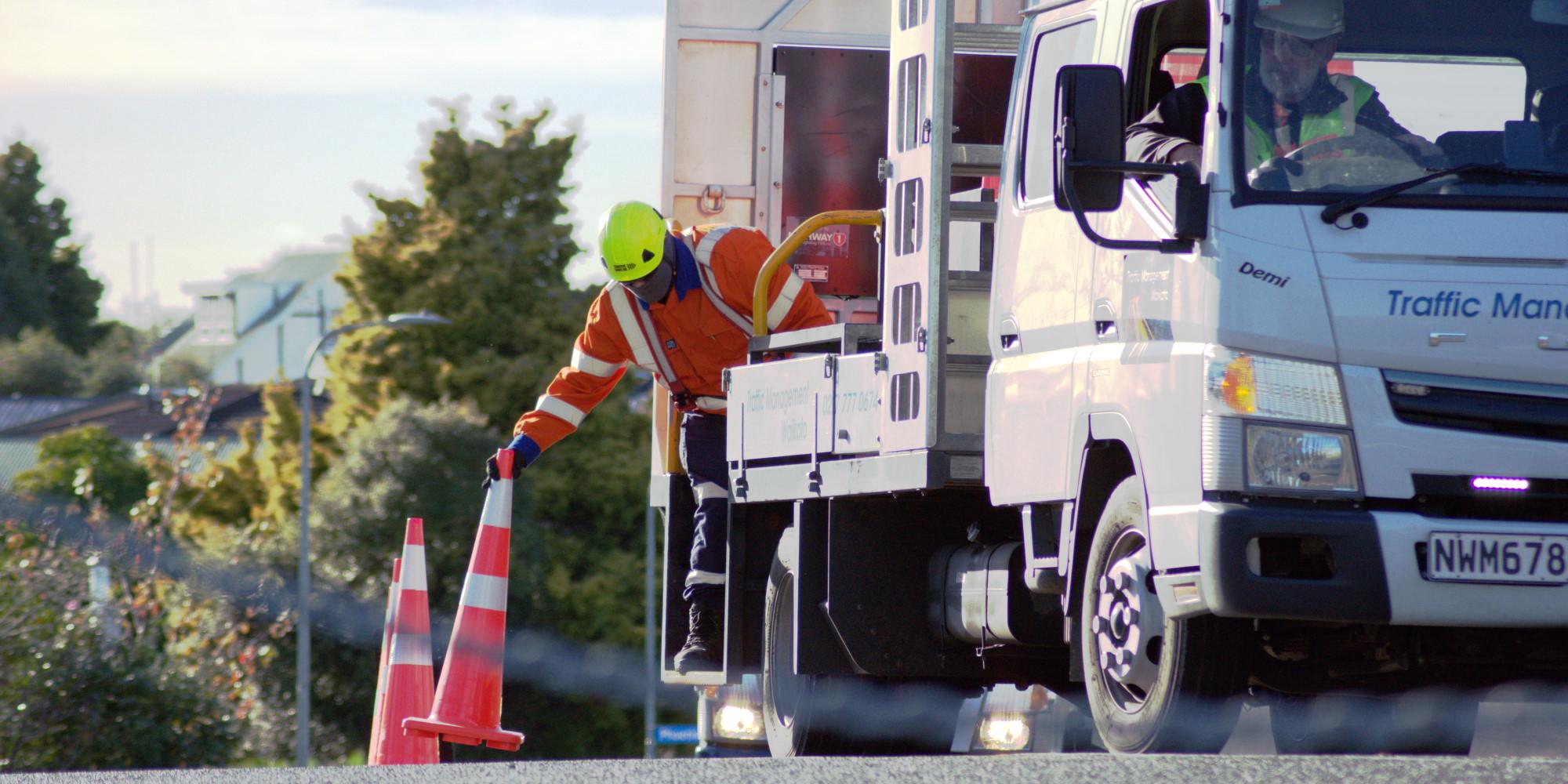 Traffic Management truck being driven as another team member sets up cones on the road from the back of the truck