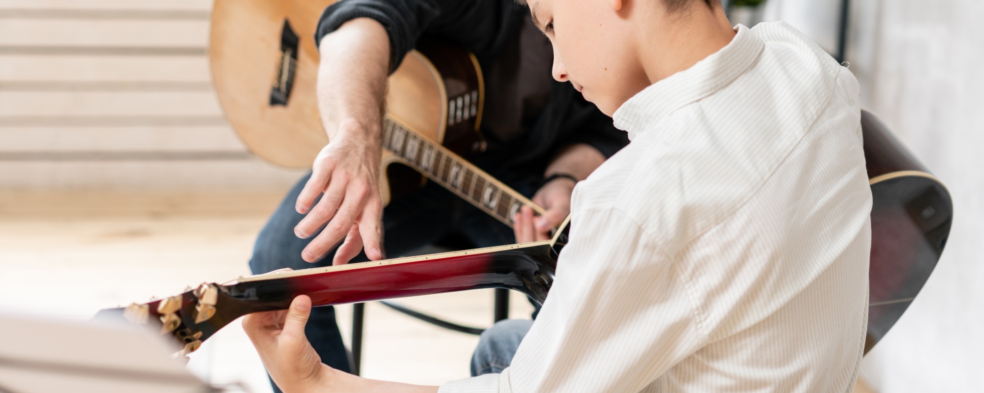 Music teacher and student with guitars while the teacher points at the right note on the students guitar