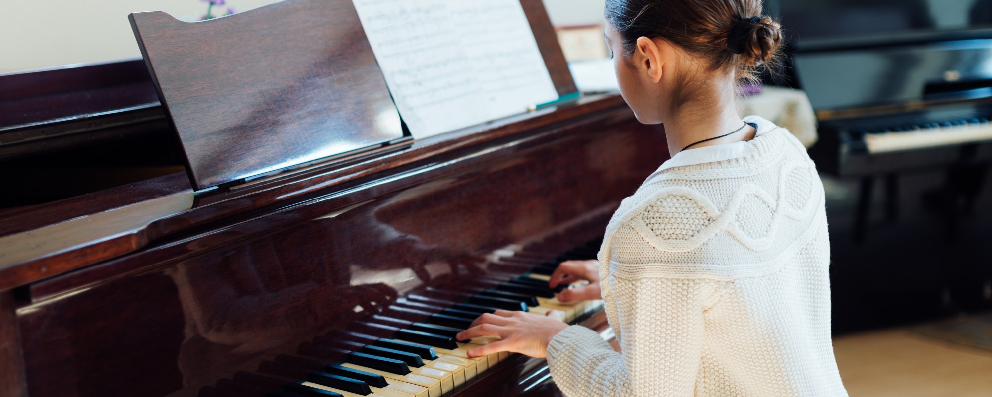 Music student practicing on a large mahogany piano in a room with another piano