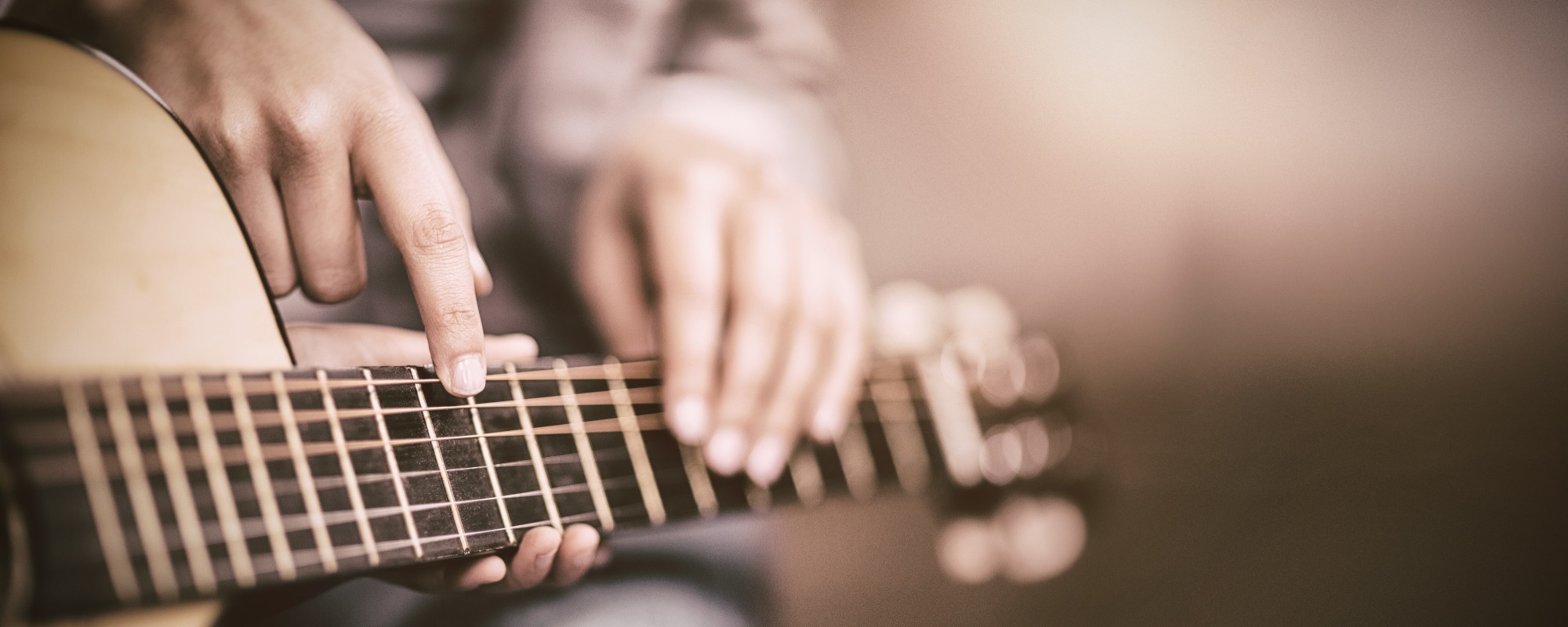 Music teacher and student sit together while the teacher points at the right note on the guitar