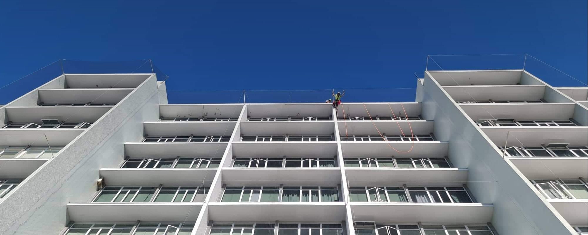 Tall, white Waikato office building with a GR Abseiling team member rappelling down from the top