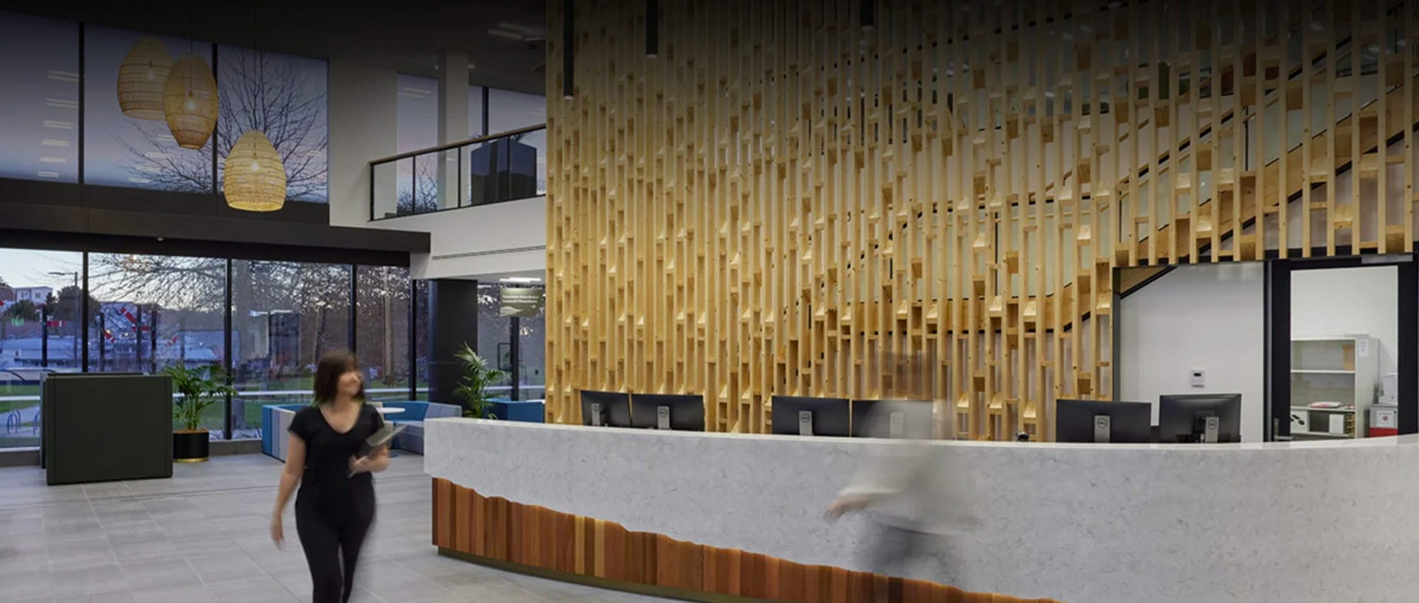 Colourform Joinery specialists walking past a beautifully crafted wooden lobby front desk backdrop