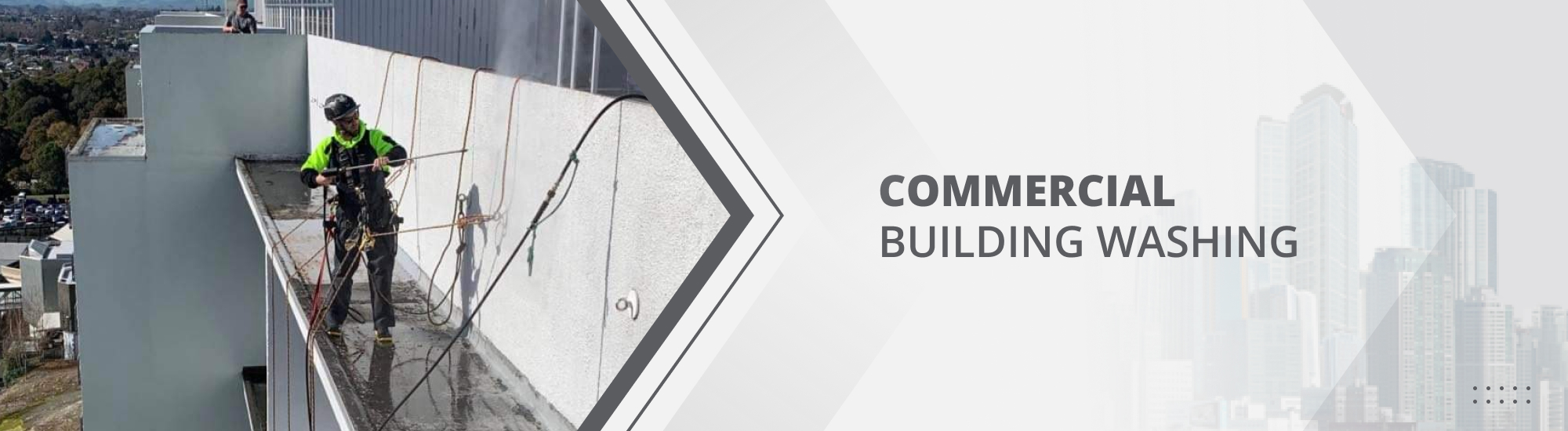 Commercial abseiler standing on the edge of a building's facade using a power washer to clean the building