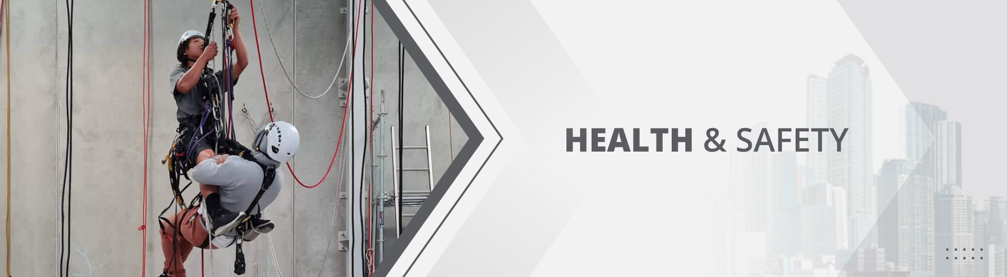 Two abseilers suspended in the air to practise and ensure health and safety as two staff members stand nearby watching