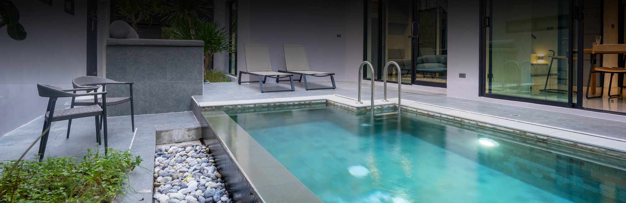 Modern white building with several outdoor accesses that lead to a stone tile backyard with a crystal clear pool