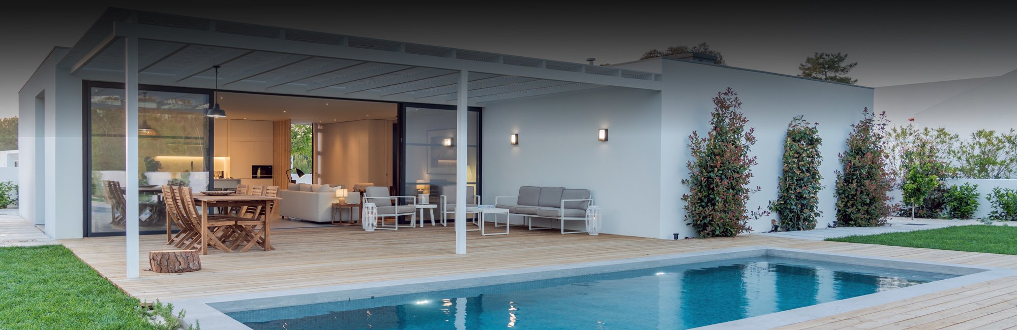 Spacious outdoor sitting areas with a clean birch wood deck under a built-on canopy beside a medium sized pool