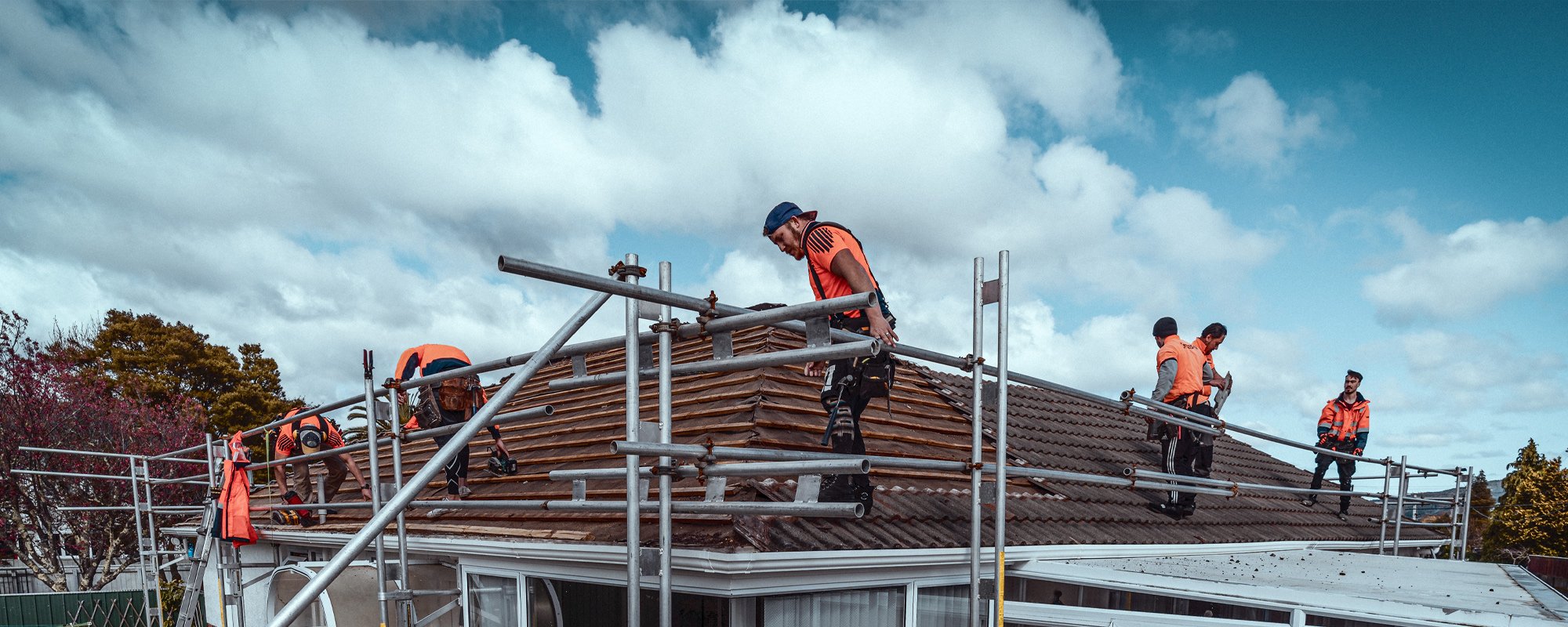 A large team of roofers in orange high-viz standing on a Wellington roof surrounded by metal scaffolding as they replace the roofing