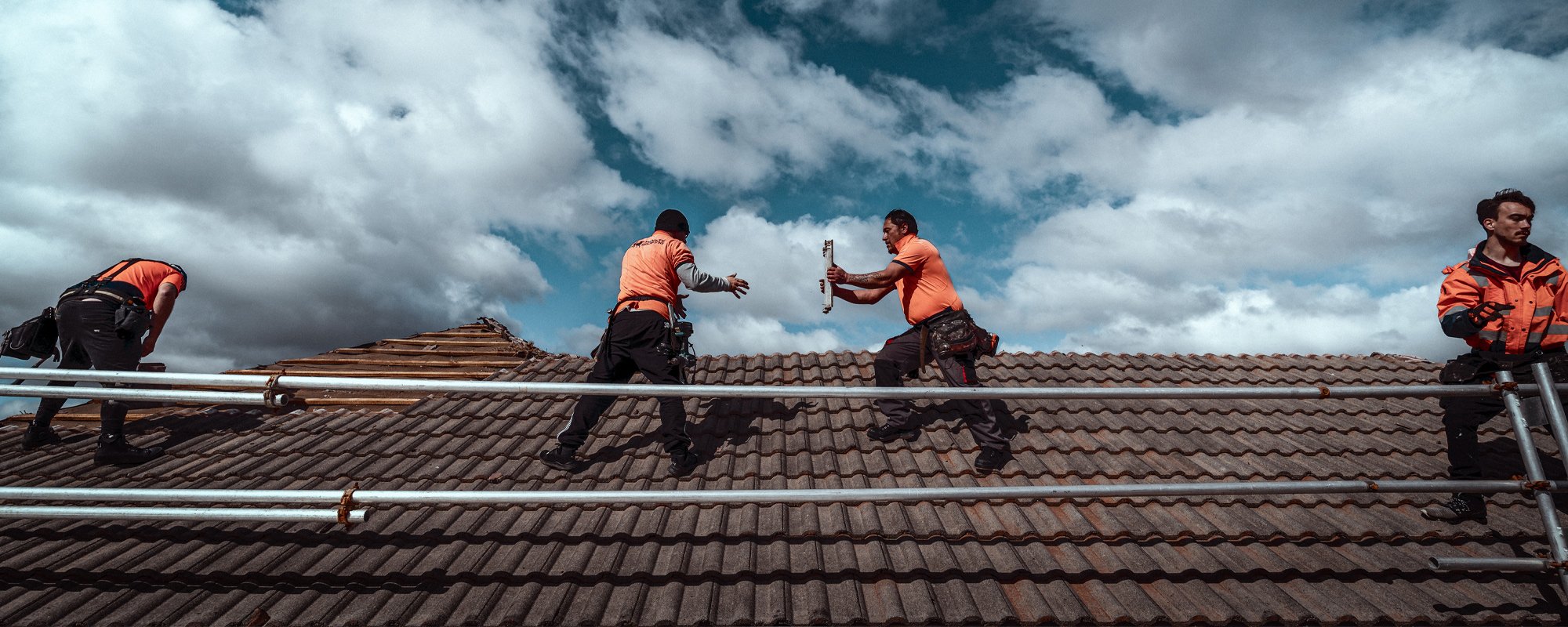 Midnite roofing team in a line formation passing roof tiles to the installer while all standing on a steep Wellington roof