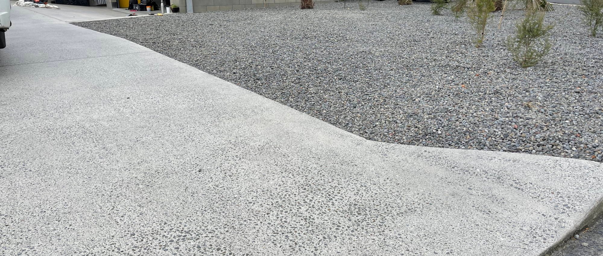 Newly paved textured concrete driveway next to a pebble garden done by Floorman Waikato