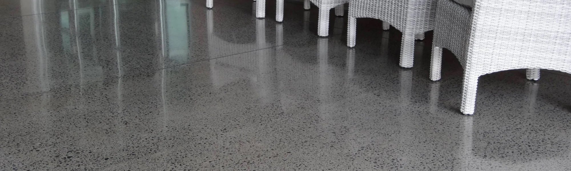 Shiny polished concrete floor outside a commercial building area with four white outdoor chairs