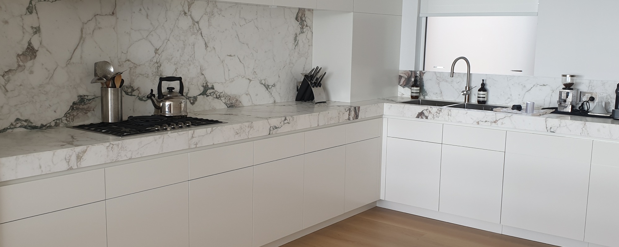 Natural thick marble benchtop with a marble splashback and white cabinets with no handles