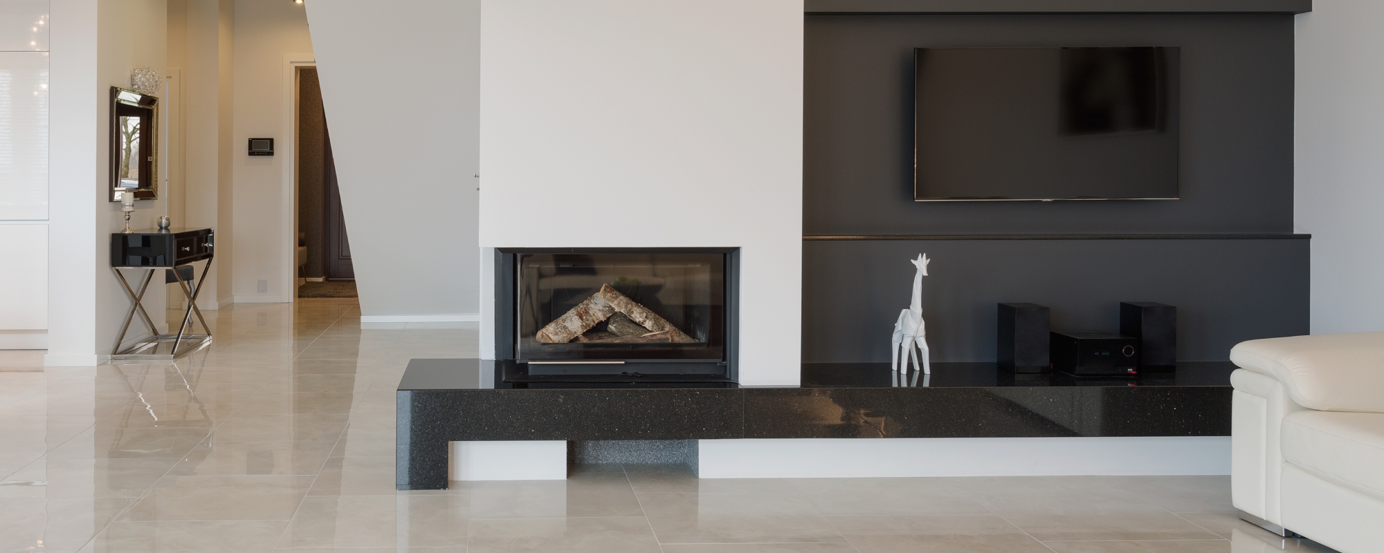Modern white painted interior with a black stone entertainment unit built in to the wall with a fireplace and stereo system on it