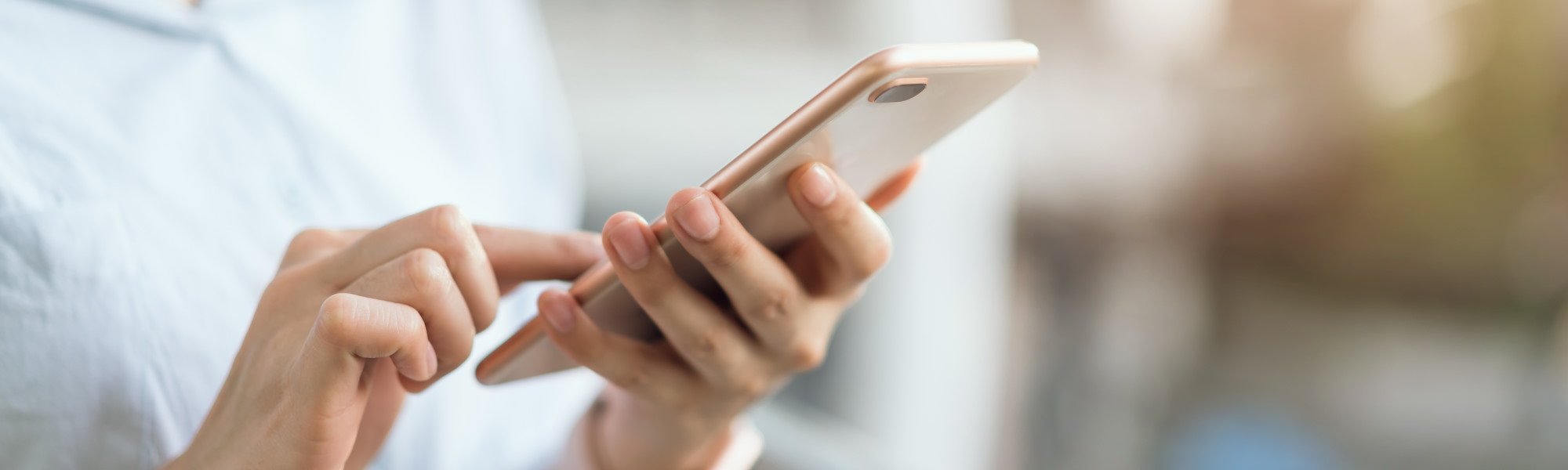 Person in a light blue shirt holding a rose gold phone while dialing in the Floorman Waikato contact details to enquire about their flooring services