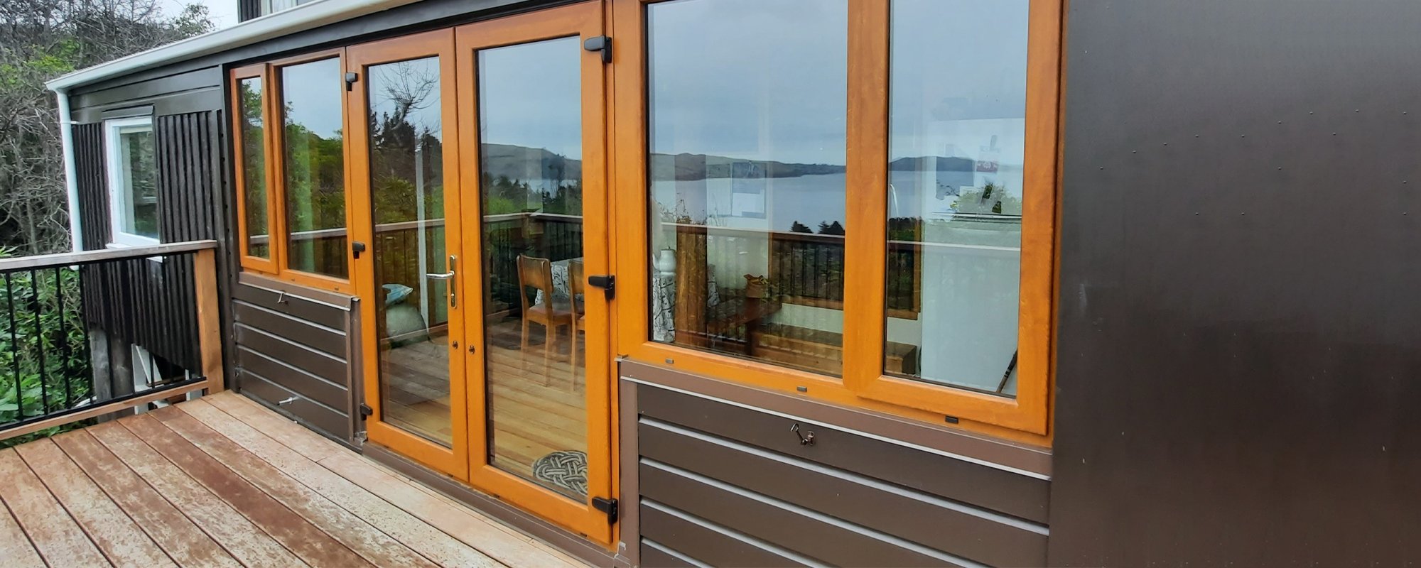 Small brown house with a wooden deck and contrasting orange uPVC window and door frames