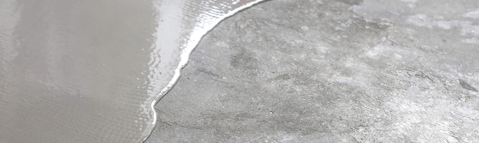 Concrete coloured liquid being spread across an old concrete floor
