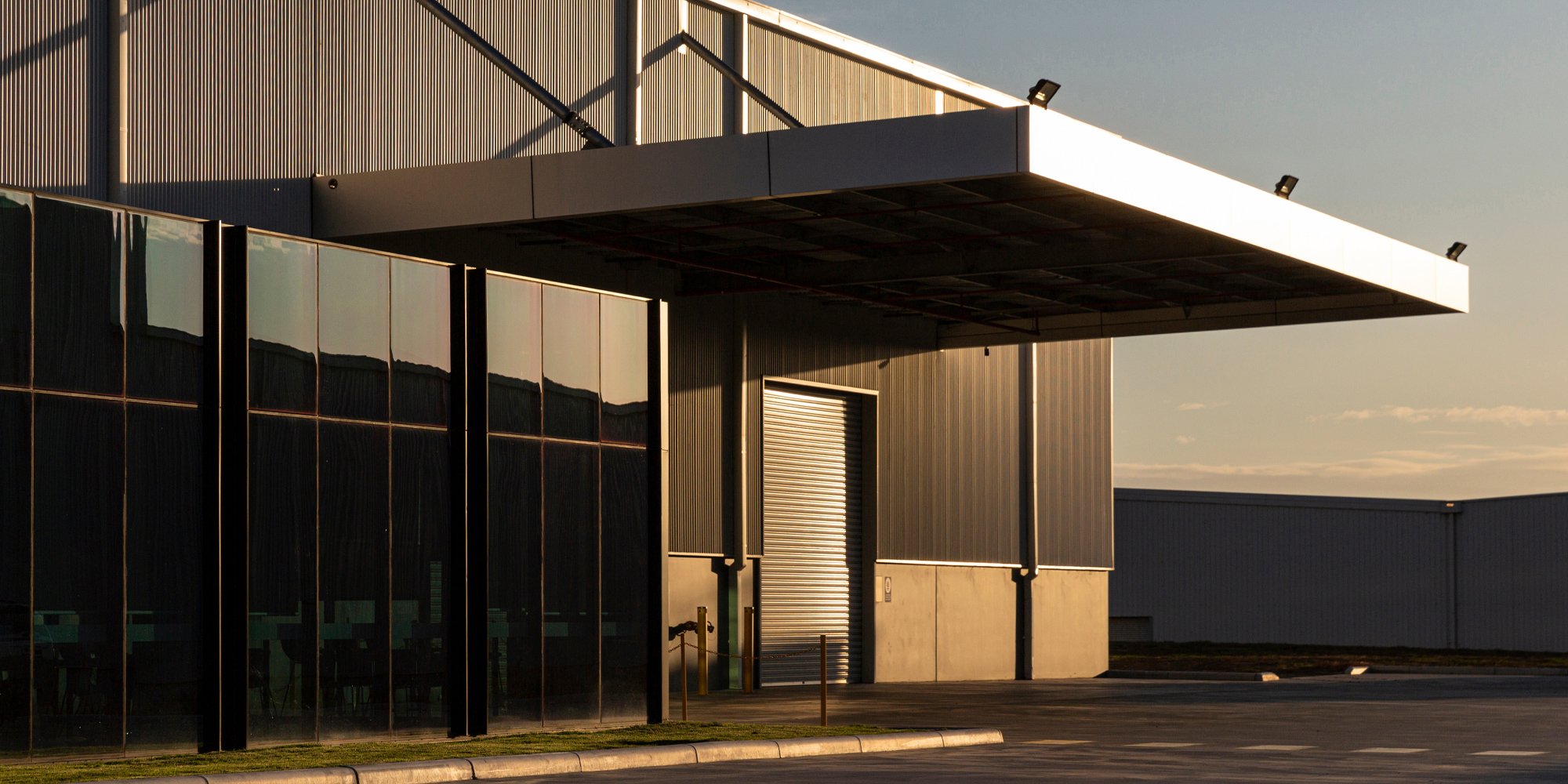 Large industrious commercial building with floor to ceiling windows, a large canopy that covers a tall commercial garage door