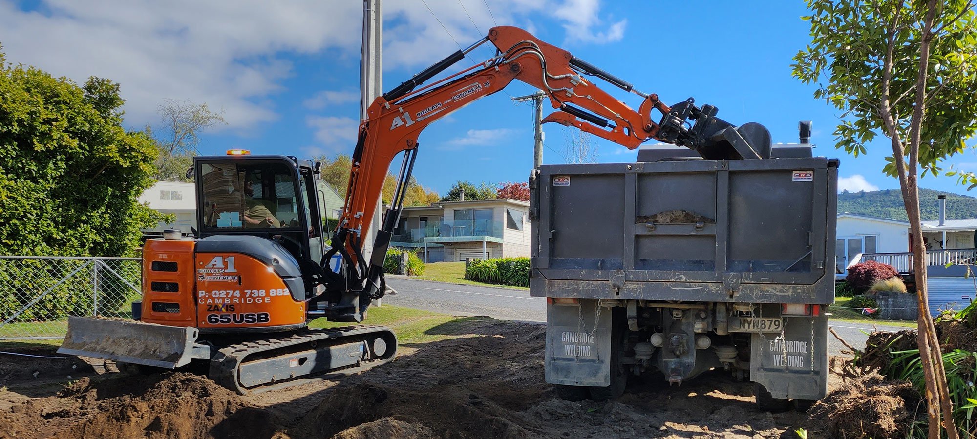 Orange earthmoving digger unloading dirt from a site they're levelling and making ready for building foundations