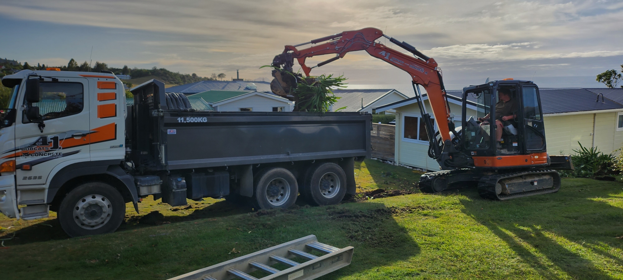 Little orange digger unloading plant debris from a site they're demolishing to unclutter the client's yard 
