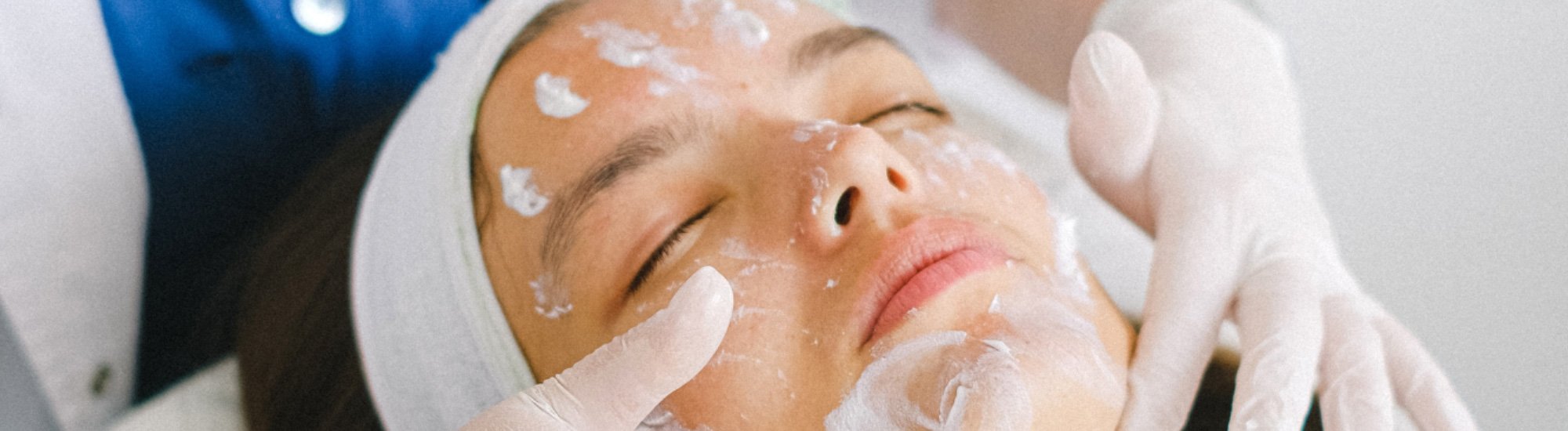 Woman laying back with a headband holding her hair back as she gets skincare product massaged all over her face
