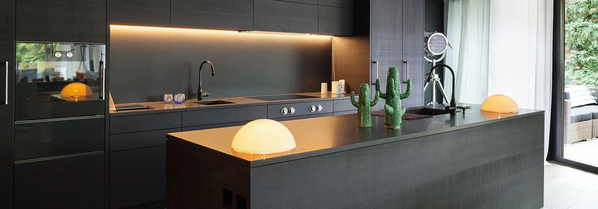Dark black kitchen with cosy yellow lighting and a family of green cacti on the island bench