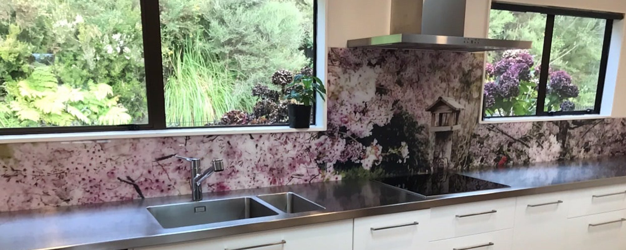 Modern white kitchen with a silver benchtop and a purple and white flowery image on the splashback