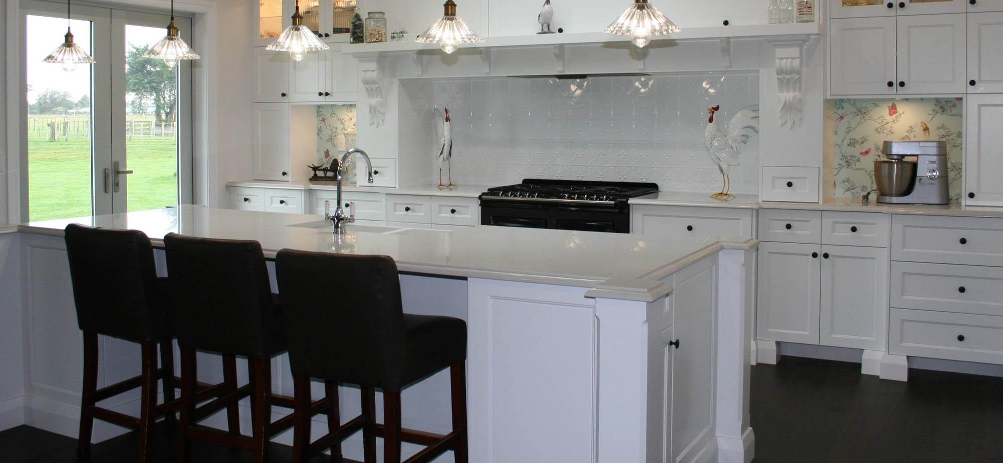 Classic white kitchen with shiny white benchtops and black cabinet handles, bar seats and a large oven