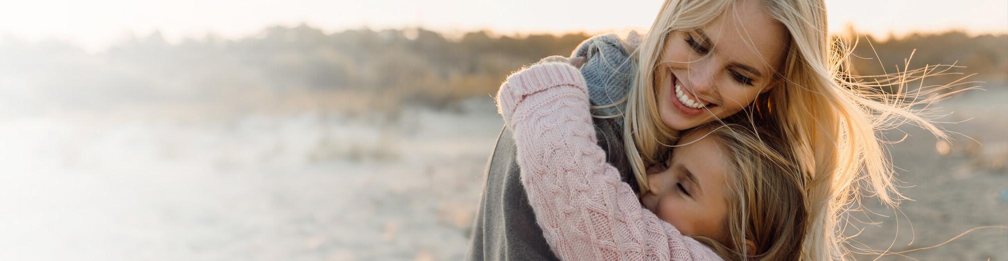 A smiling mother hugging her daughter at the beach