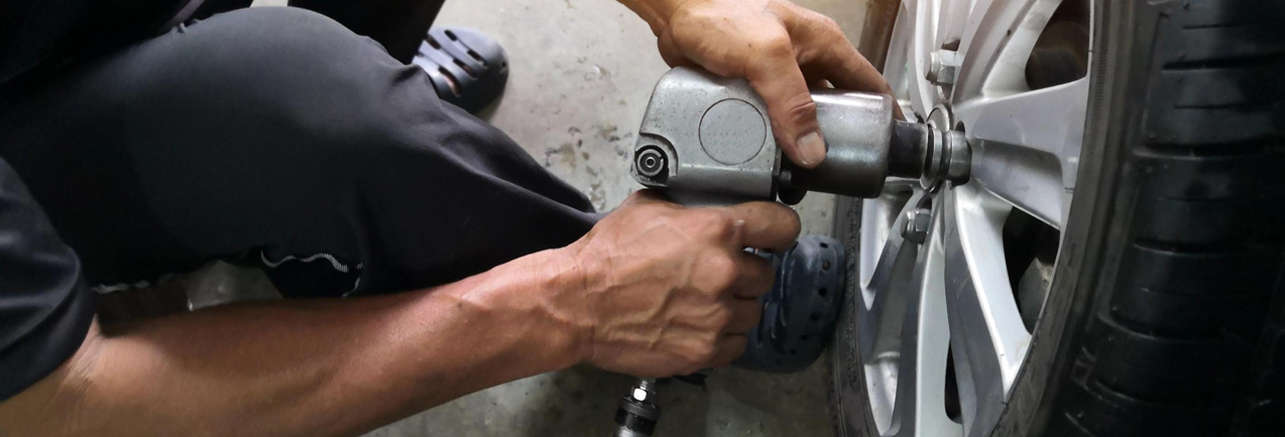 Motor Works Group team member using a powered tool to take off a wheel's lug nuts