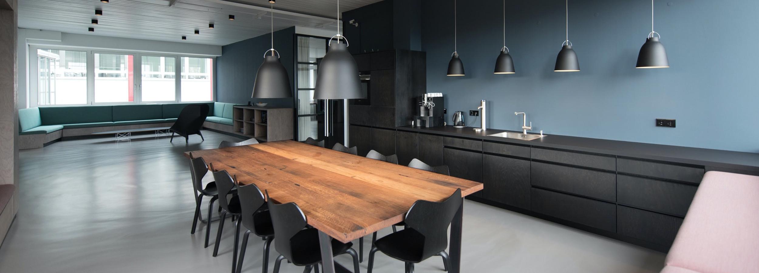  Modern kitchen with a matte blue painted wall, sleek black painted cabinetry, 10 seat dining table with a fine wood top