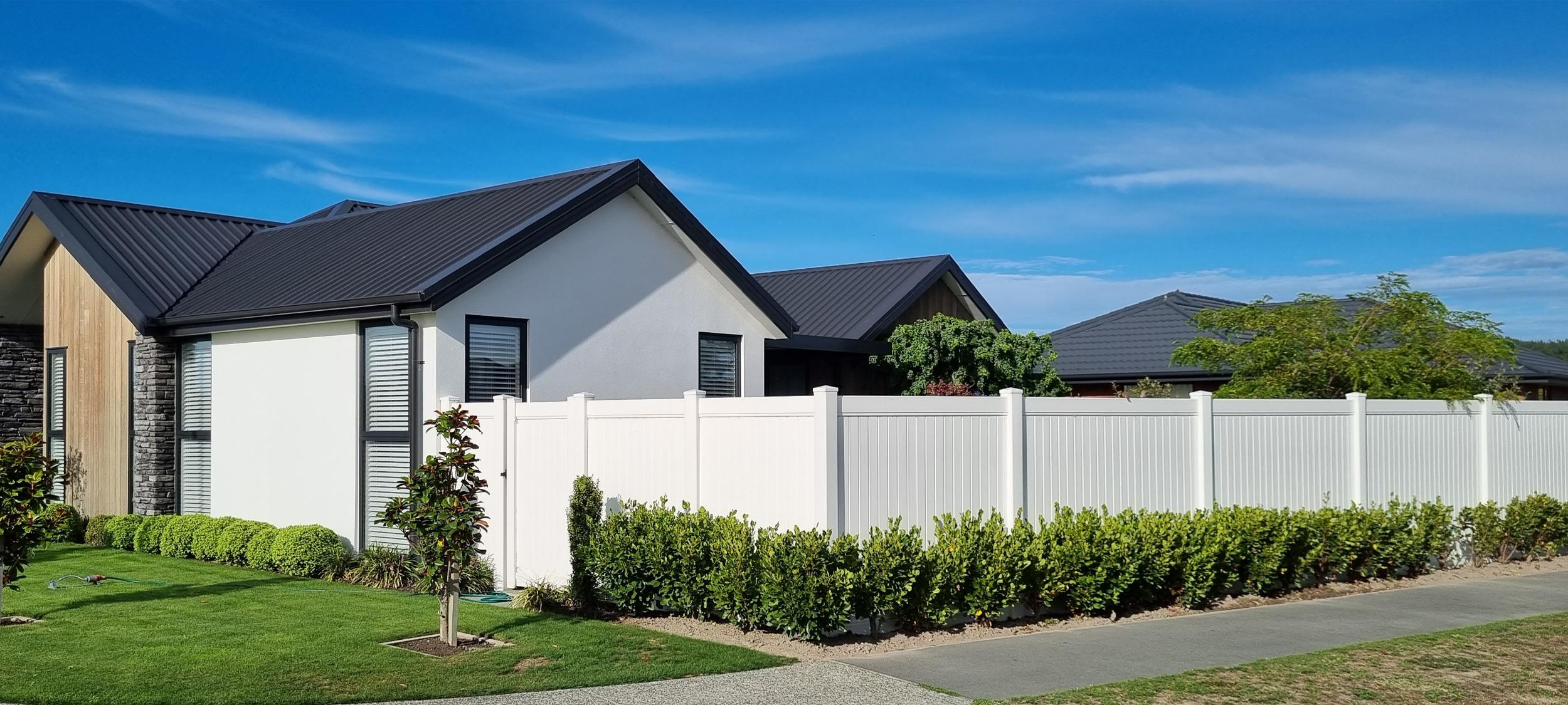 Modern home with a vibrant green garden and bushes alongside a tall white spotless fence