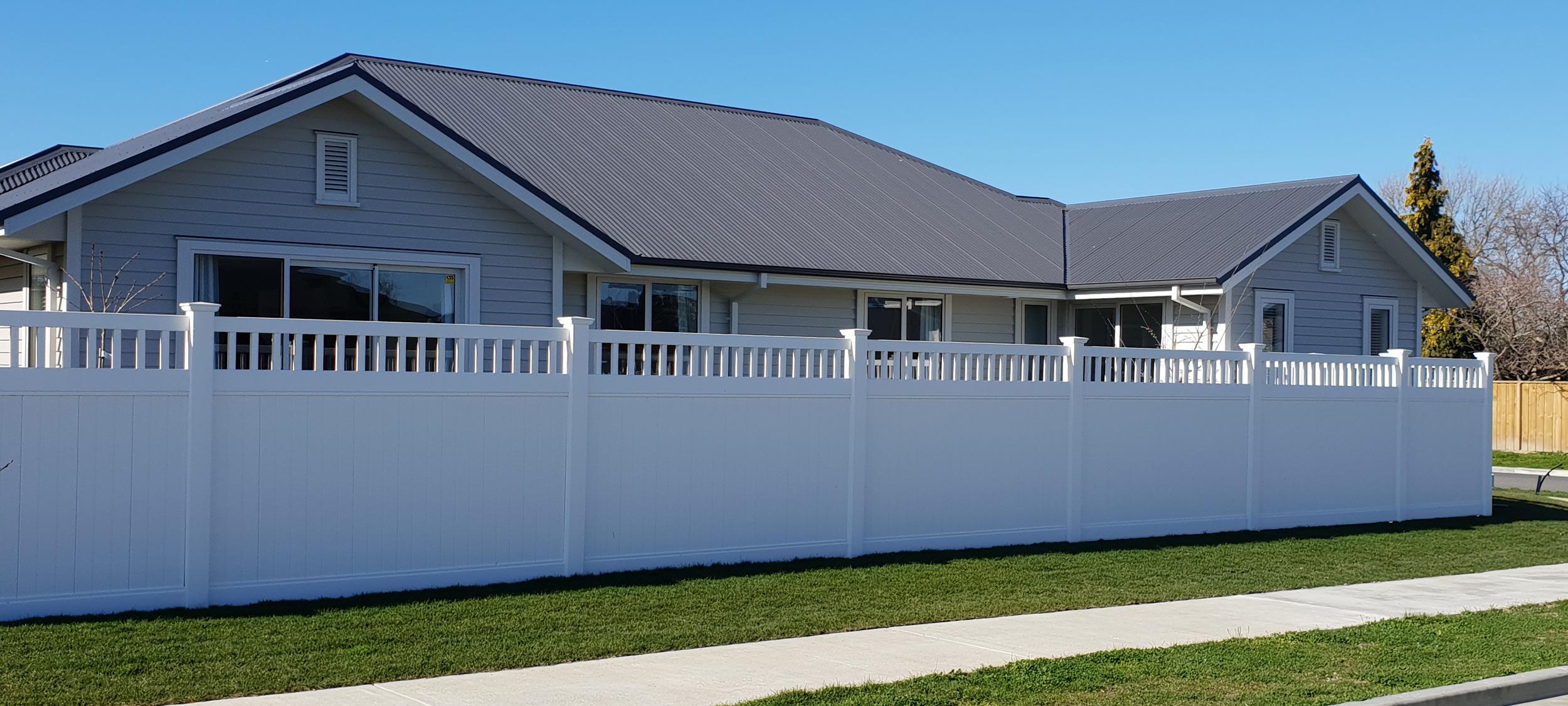 Tall new white fence in front of a grey modern house with a tidy front lawn and recently poured footpath