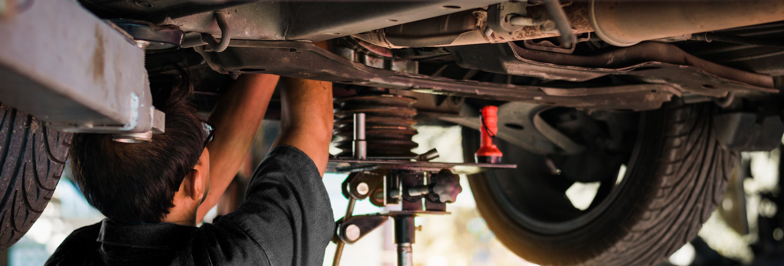Motor Works Group team member under an elevated vehicle, performing a vehicle service