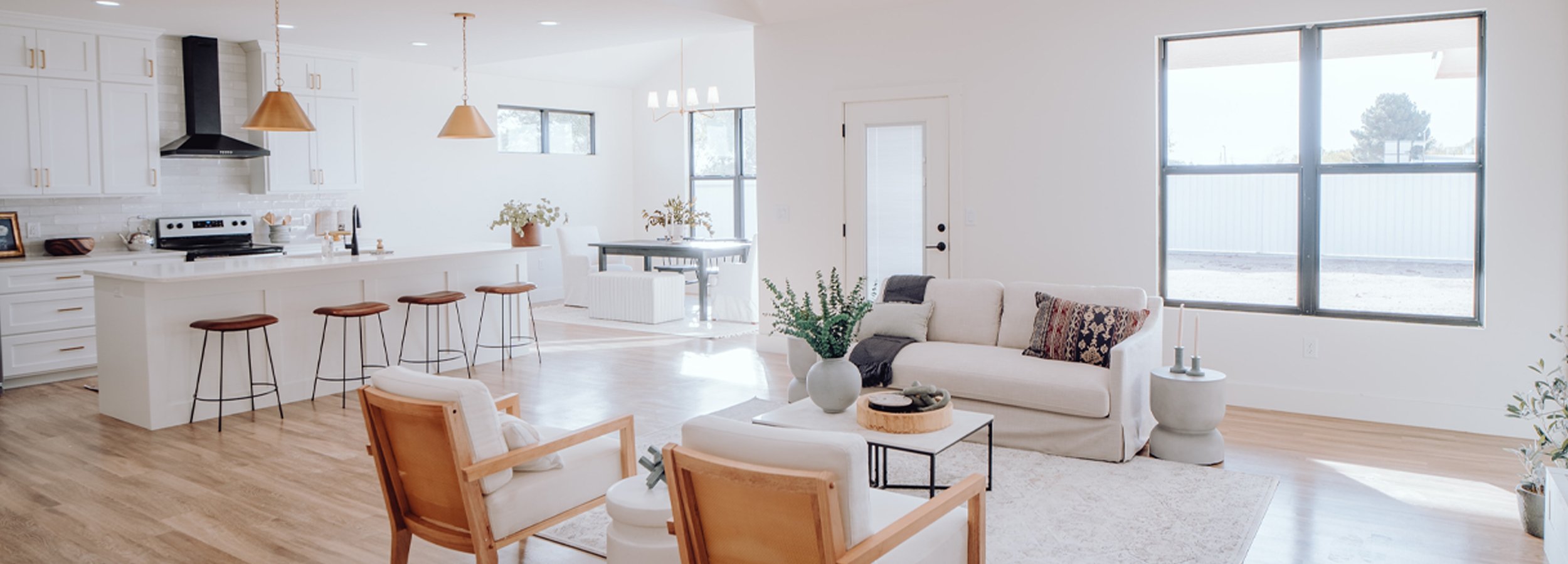 Cosy minimalistic living room and kitchen area painted in a serene white with large open windows letting in heaps of natural light
